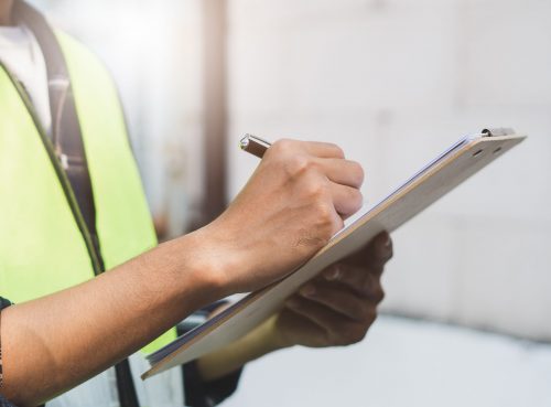close up hands of inspector waer safety vest and checking list into clipboard